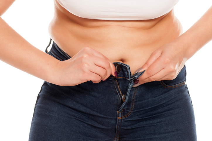 a young woman has difficulty buttoning her jeans